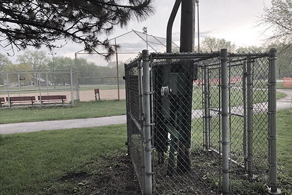 A strut and backboard system inside a fenced off area next to a baseball field.