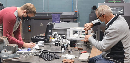 Two Milbank employees work on electrical equipment spread out across a table.