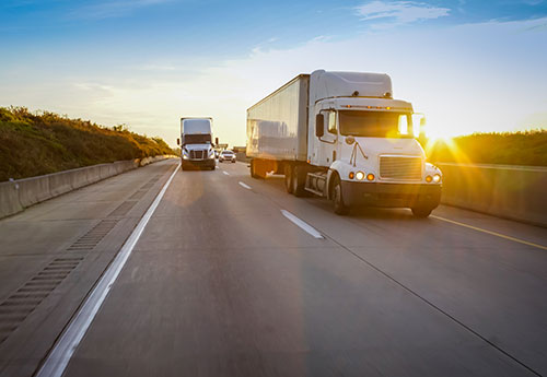 Two trucks drive down the highway carrying manufacturing products to clients.