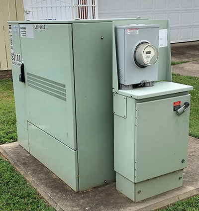 A Milbank meter socket is attached to a green transformer outside a house.